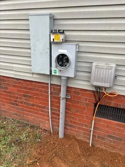 Exterior electrical meter and service equipment mounted above a brick foundation
